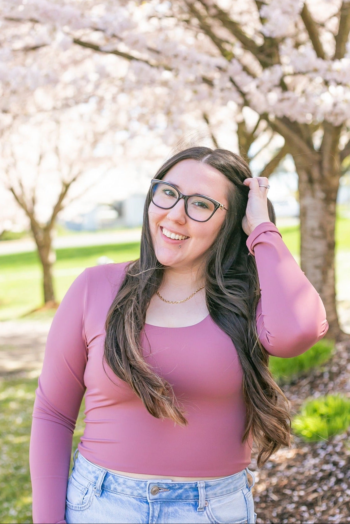 Woman with glasses posing in front of cherry blossom trees